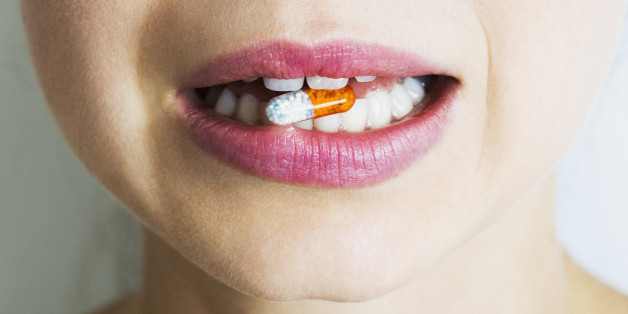 Woman biting multi coloured medical capsule